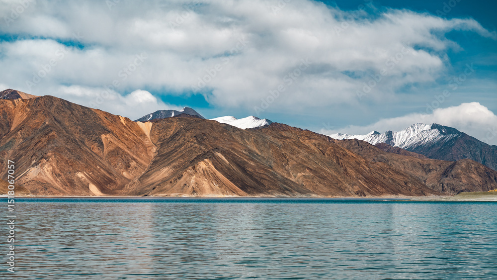 Obraz premium Scenic view of Pangong Lake surrounded by majestic brown mountains under a clear blue sky, reflecting pristine waters, creating a serene and picturesque high-altitude Himalayan landscape in Ladakh