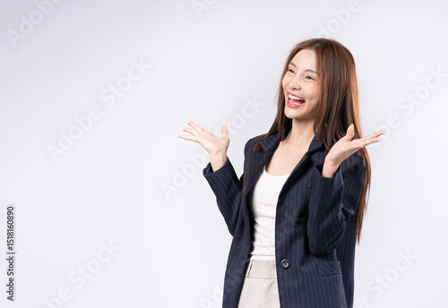 Beautiful Asian woman in suit raising both hands showing product presentation with confidence and friendly smile.