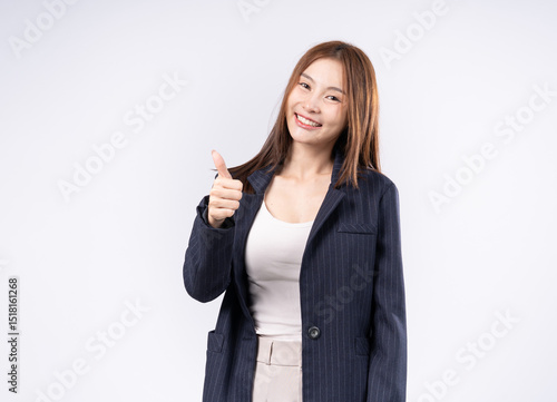 Portrait of beautiful Asian woman in suit giving thumbs up gesture as like, smiling face, white background photo in studio.