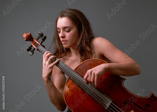 Young woman musician playing cello on gray background