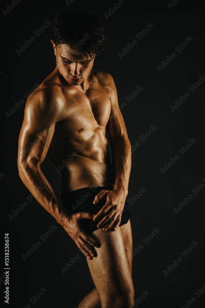 Naklejka premium Fit young man displaying his muscular physique against a dark background, showcasing strength and fitness.