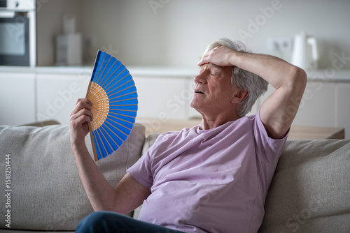 Fotografía Elderly man feeling dizzy and unwell from heat, fanning himself at home without cooling system