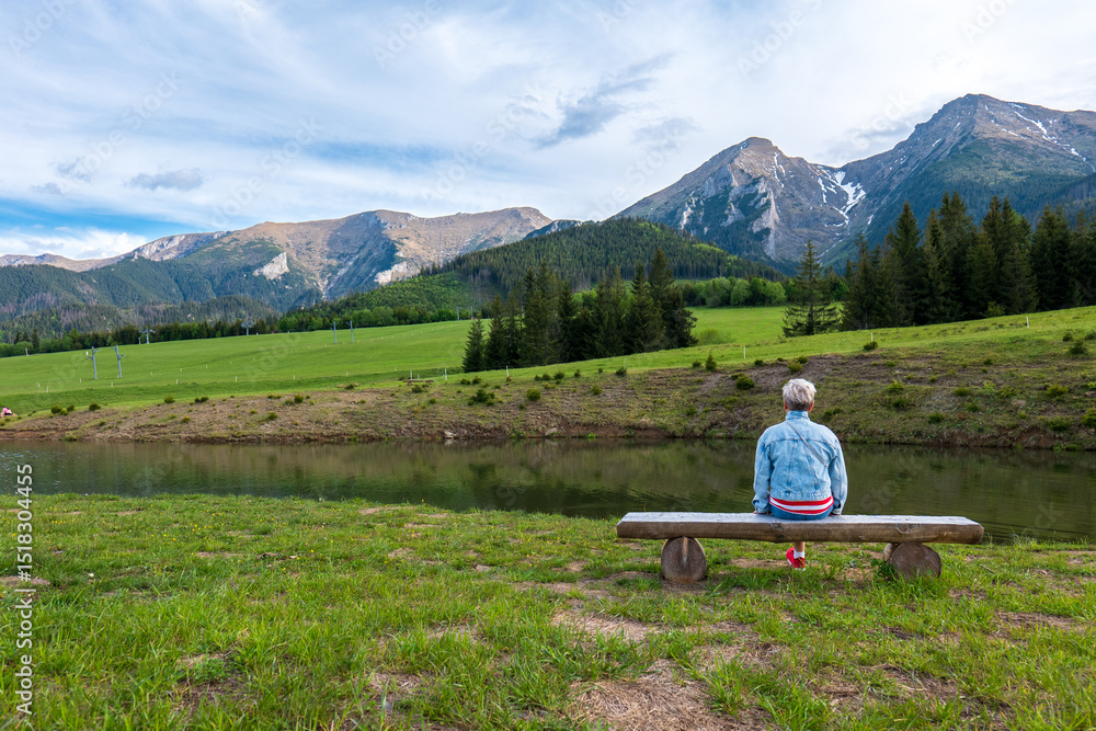 Person sitting on a bench facing the High Tatras above Ždiar, Slovakia, by a calm pond. A tranquil moment of reflection in scenic alpine nature. Person sitting on a bench facing the High Tatras above Ždiar, Slovakia, by a calm pond. A tranquil moment of reflection in scenic alpine nature.