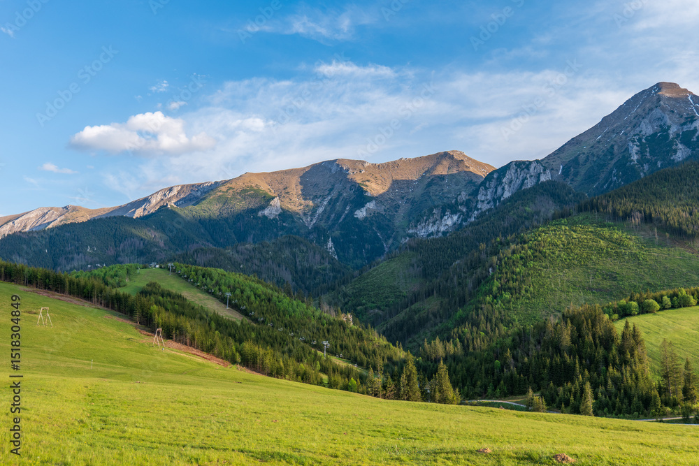 Panoramic view of the High Tatras above the village of Ždiar, Slovakia, with green meadows, forests, and ski lift structures under a clear spring sky. Panoramic view of the High Tatras above the village of Ždiar, Slovakia, with green meadows, forests, and ski lift structures under a clear spring sky.