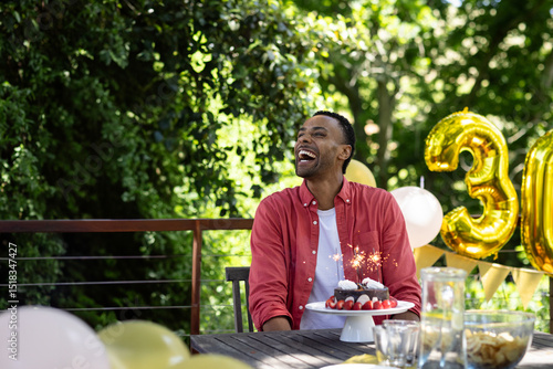 Принти на полотні African American man sitting at patio table celebrating thirtieth birthday with