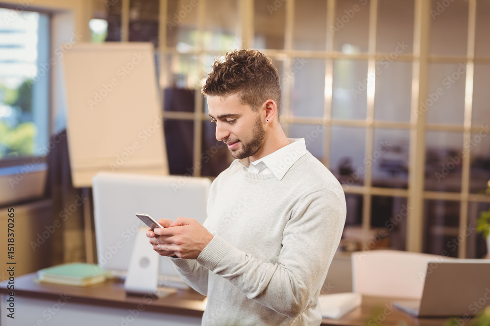Man wearing sweater standing and checking smartphone in modern office with desk and monitor Man wearing sweater standing and checking smartphone in modern office with desk and monitor