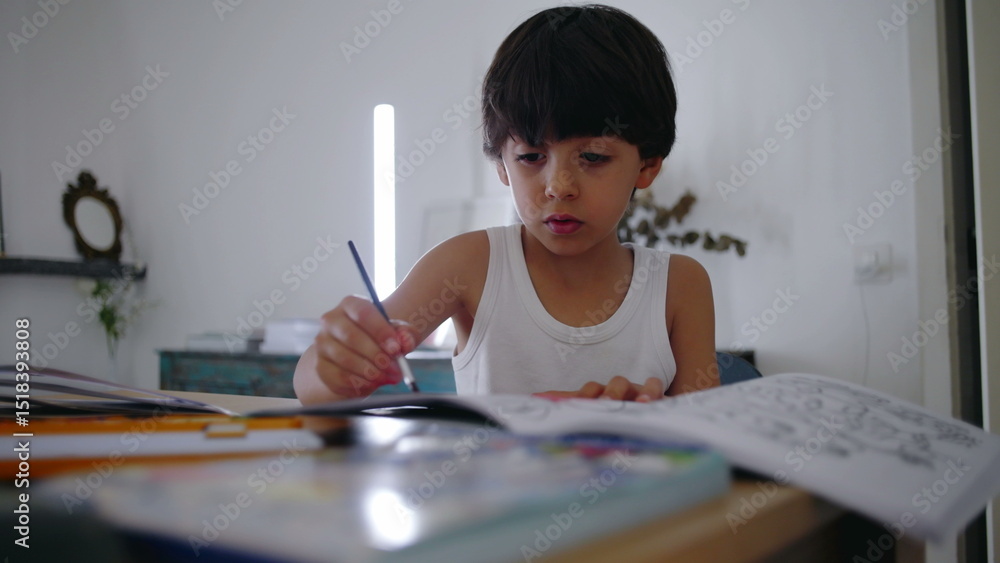 Young boy sitting at table, focused on coloring and drawing in a book, engaging in creative play and developing fine motor skills during early childhood in a calm home setting Young boy sitting at table, focused on coloring and drawing in a book, engaging in creative play and developing fine motor skills during early childhood in a calm home setting