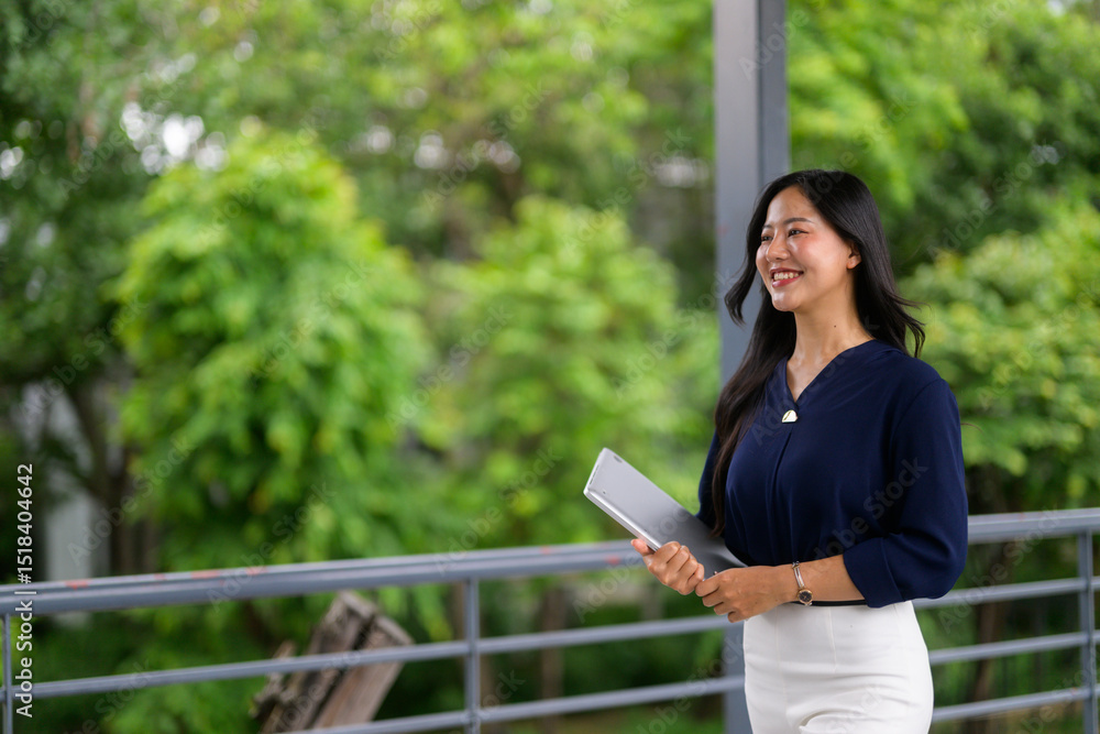 Fototapeta premium Young businesswoman smiling and walking in green corridor holding tablet