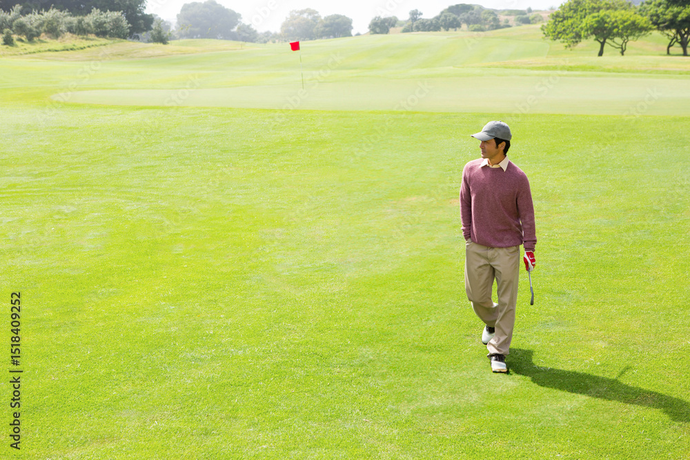 Fototapeta premium Golfer walking across vibrant green fairway toward red flag, holding putter with red glove