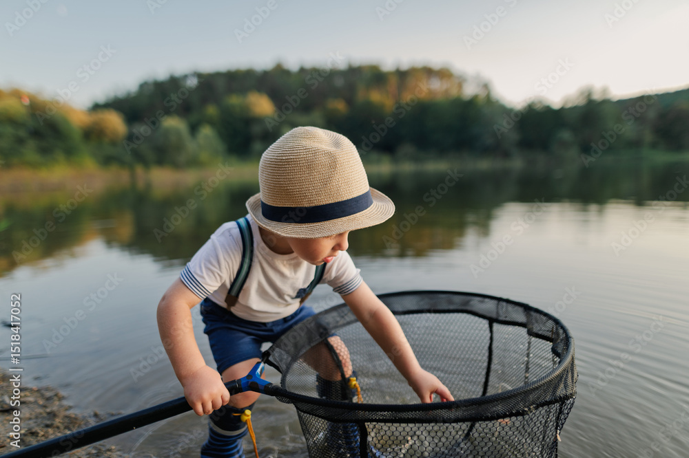 Obraz premium Boy playing with fishing net by the lake, enjoying a carefree moment in nature.