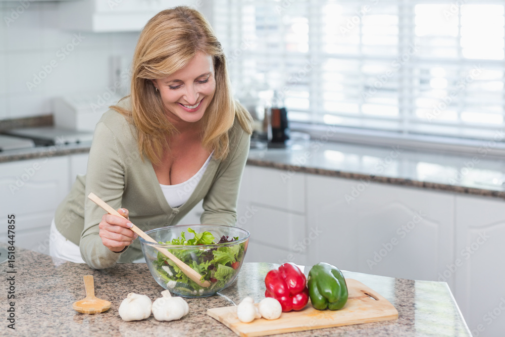 Middle-aged white woman stirring salad in glass bowl at kitchen counter, copy space Middle-aged white woman stirring salad in glass bowl at kitchen counter, copy space