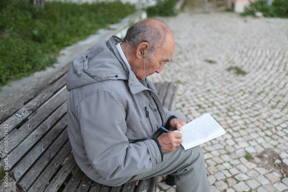 Fototapeta premium Elderly man writing on notebook while sitting on bench