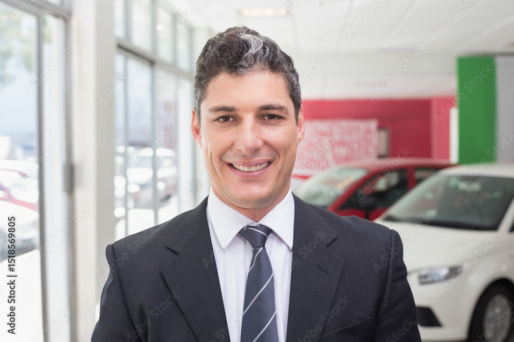 Middle-aged man wearing suit and striped tie standing by display cars in showroom by glass windows Middle-aged man wearing suit and striped tie standing by display cars in showroom by glass windows