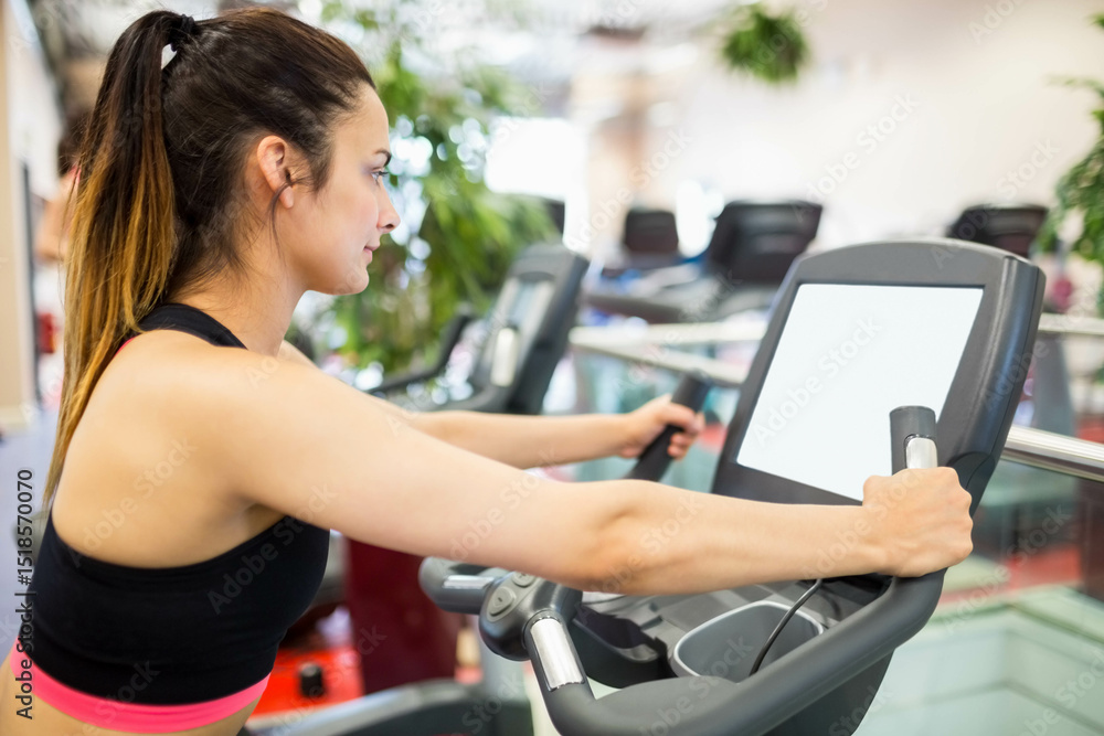 Female fitness enthusiast gripping elliptical handles monitoring digital console at gym, copy space Female fitness enthusiast gripping elliptical handles monitoring digital console at gym, copy space