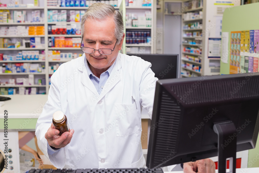 Prescription bottle resting on counter beside computer monitor and stocked medication shelves Prescription bottle resting on counter beside computer monitor and stocked medication shelves