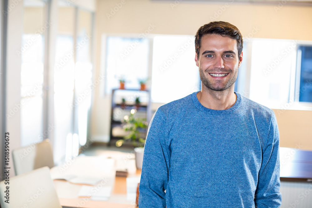 Man in his 30s smiling at camera in office with wooden table, scattered papers, copy space