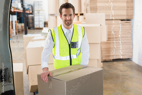 Fotografie Male worker standing in warehouse behind cardboard box at delivery van rear wear