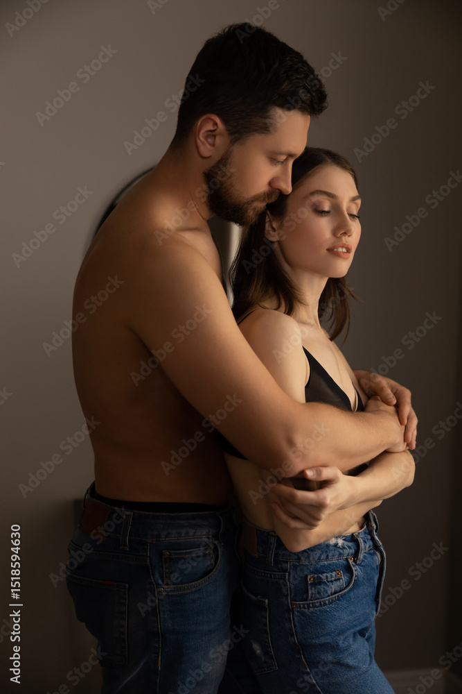 Shirtless man in jeans embracing woman in black top and jeans standing closely in intimate moment Shirtless man in jeans embracing woman in black top and jeans standing closely in intimate moment