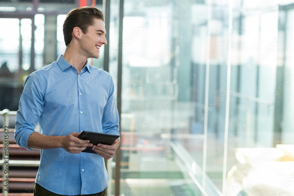 Fototapeta premium Man wearing blue shirt standing in office corridor holding tablet and smiling to left, copy space