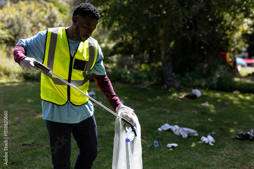 Photos African American man picking up litter in park with metal picker and plastic-lin