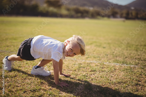 Принти на полотні Boy crawling in plank pose on grass sports field wearing sneakers under sunshine