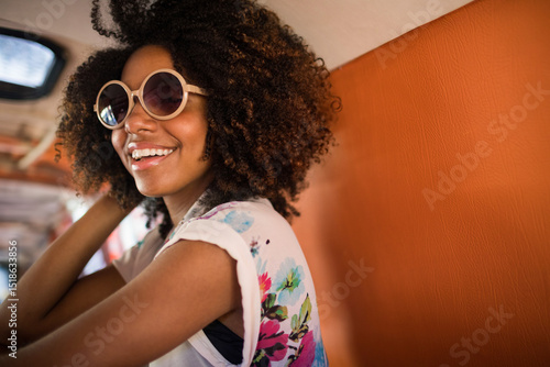 African American woman sitting in retro van on orange seat, wearing floral T-shirt and sunglasses