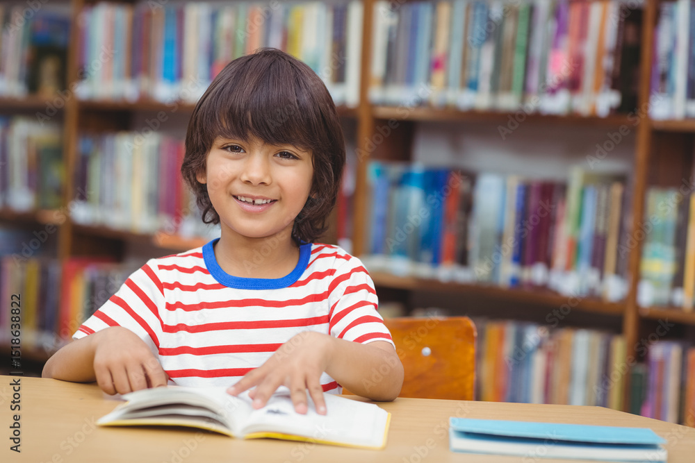 Boy wearing red-and-white striped T-shirt sitting at library table reading book by bookshelves Boy wearing red-and-white striped T-shirt sitting at library table reading book by bookshelves