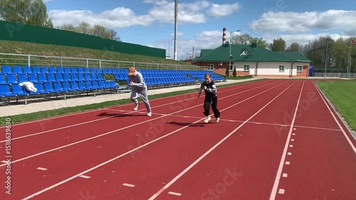 Father and daughter are running around the stadium. A man is racing with a girl.