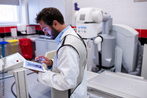 Fototapeta X-ray machine standing ready in hospital radiology room, with digital console an