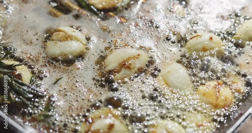 barbecue party, garlic and thyme languish in butter in a frying pan for meat steaks, oil bubbles are illuminated by firelight, close-up footage of grilling steaks