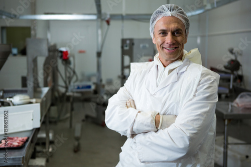 Male wearing lab coat inspecting raw meat trays on conveyor belt in food plant, copy space