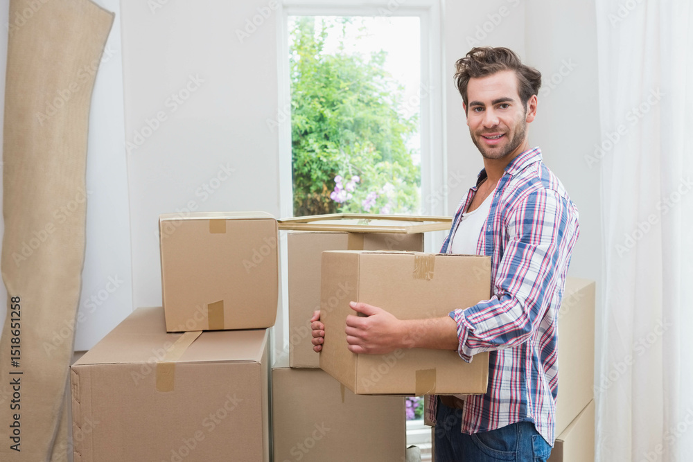 Man in his twenties in plaid shirt standing surrounded by moving boxes at home, copy space Man in his twenties in plaid shirt standing surrounded by moving boxes at home, copy space