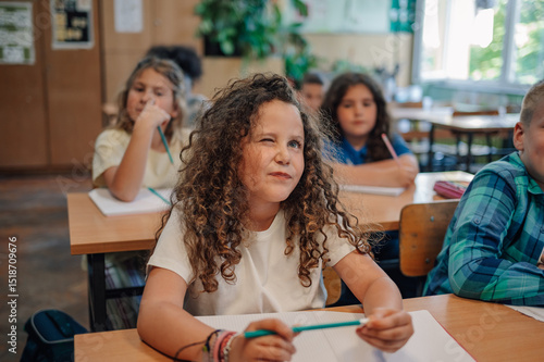 Fotografie Curious girl winking and thinking during class at elementary school