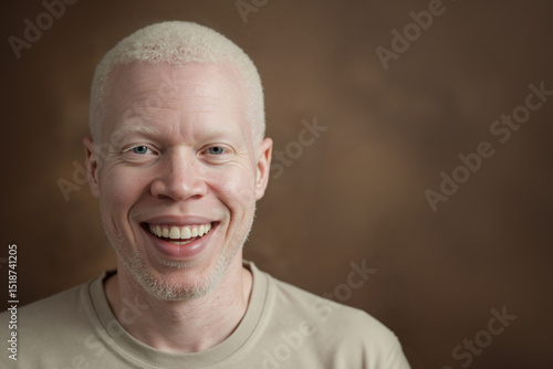 Happy middle-aged albino man with albinism and white hair smiling at camera against brown background with copy space.