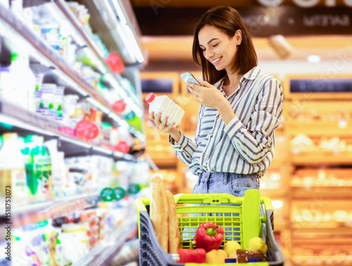 Принти на полотні Smiling young woman taking dairy products from shelf in the supermarket, holding