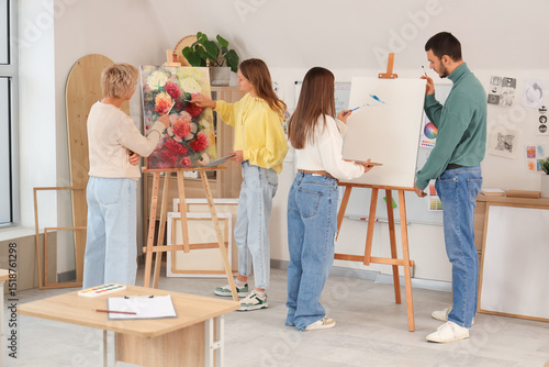 Young students with teacher painting on canvas in art school