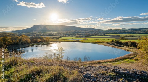 Fototapeta Naklejka Na Ścianę i Meble -  A peaceful rural landscape featuring a dam and reservoir, with farmland and fields visible in the distance, under a bright, sunny sky