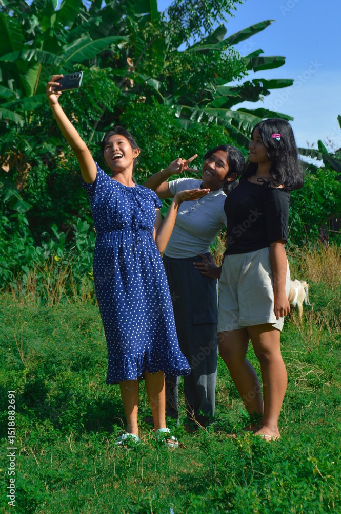 Fototapeta premium They strike another pose while snapping a selfie together, goats grazing in the background.