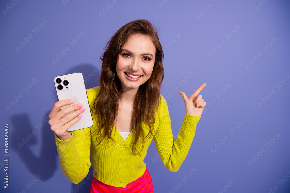 Cheerful young woman in trendy yellow cardigan holding smartphone while gesturing on a purple background Cheerful young woman in trendy yellow cardigan holding smartphone while gesturing on a purple background