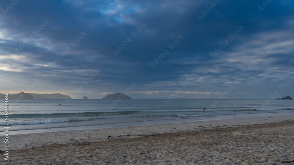 Beautiful sandy beach. A tropical island. The waves of the turquoise ocean are calmly rolling towards the shore. Silhouette of man in the water. Mountains on the horizon against the sky, clouds. Beautiful sandy beach. A tropical island. The waves of the turquoise ocean are calmly rolling towards the shore. Silhouette of man in the water. Mountains on the horizon against the sky, clouds.