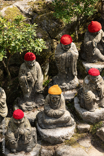 The stone Buddha statues with red knitted hats outdoor in the Japanese garden at the Daisho-in temple at daytime on Miyajima island near Hiroshima in Japan.
