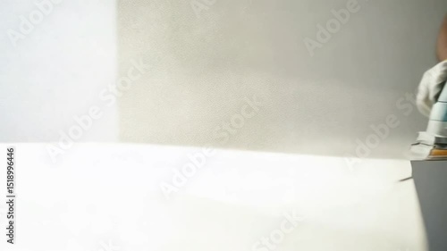 Construction worker sanding drywall with orbital sander wearing protective gloves