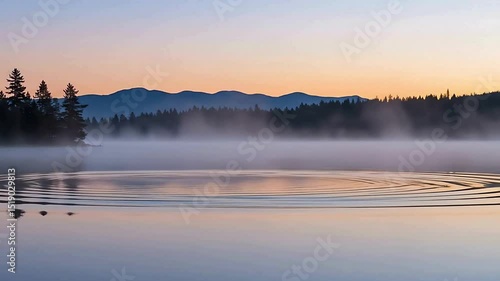 lake with a reflection of pine trees and mountains in the background and early morning mistdrifting over the water