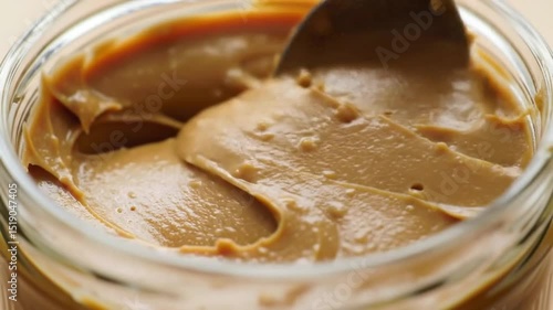 Creamy peanut butter in a glass jar with a spoon, showcasing its smooth texture and rich color