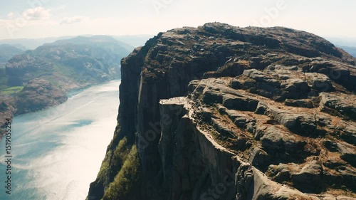 Iconic Preikestolen towers over still deep waters of Lysefjord. Rugged texture of rock and expansive panoramic view of Norwegian wilderness