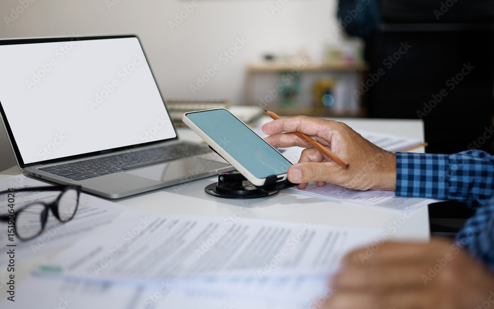 asian man using smart phone working on desk review documents report and meeting online via laptop at home, work from home concept asian man using smart phone working on desk review documents report and meeting online via laptop at home, work from home concept