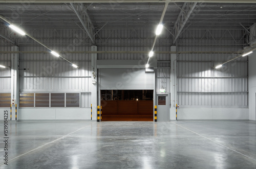 Concrete floor and shutter door inside industrial building at night. To construction for factory or warehouse. New clean and shiny surface. Nobody and empty space suit for product display background.