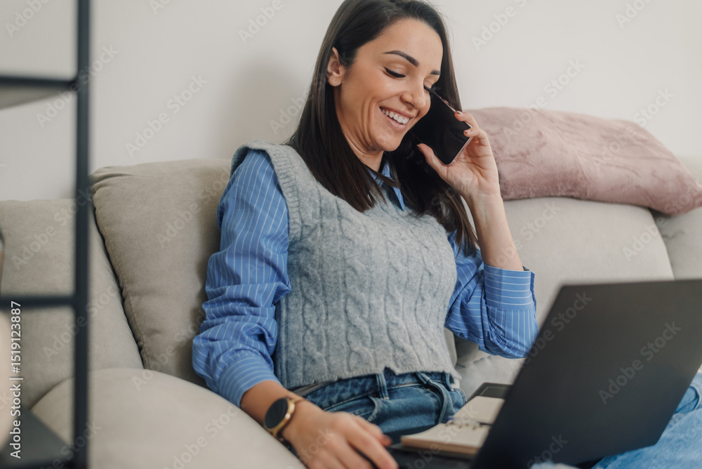 © Ljustina - Smiling freelancer working from home on sofa with laptop and phone