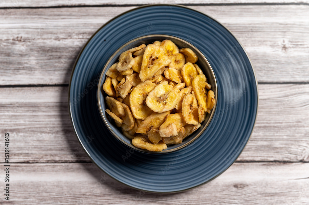 Dried banana slices arranged in a blue bowl placed on a wooden surface, A natural and healthy snack in a rustic setting.healthy food