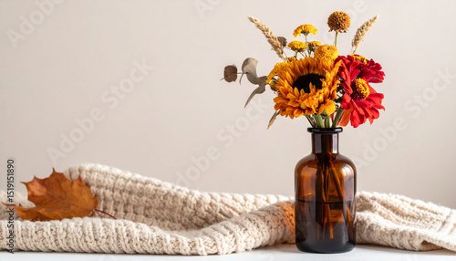 the image showcases a small amber colored glass vase filled with an assortment of autumnal blooms and dried wheat stems